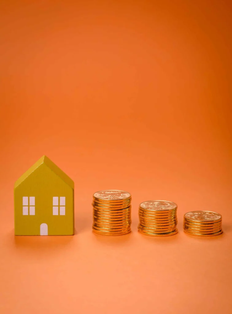 Helical Piers for Decks - A Small Wooden House Model with Change Stacked Beside It On an Orange Background