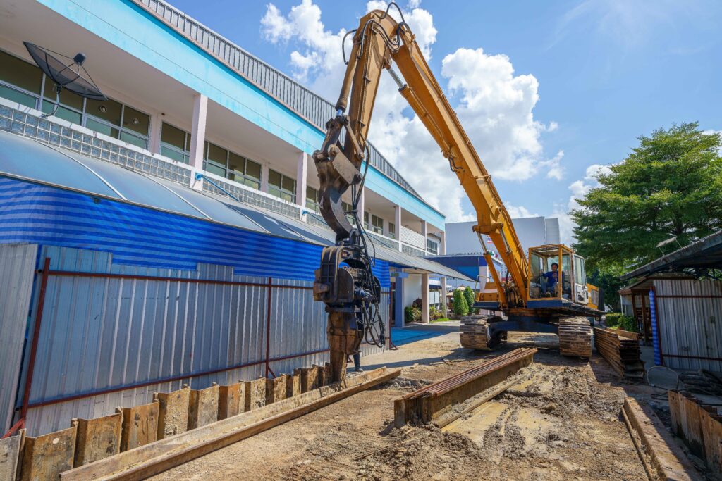 Steel Sheet Pile Installation - A Tractor Installing Sheet Piles Near a Commercial Building