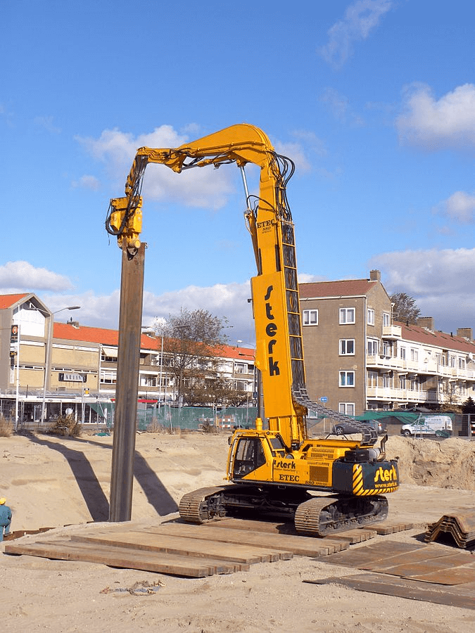 Sheet Pile Retaining Wall Guide - An Excavator-Mounted Sheet Pile Driver Installing Sheet Piles