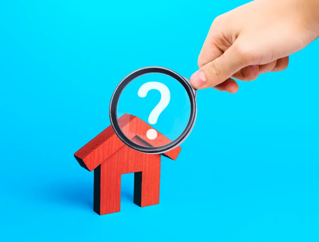 Can a Slab Foundation Support a Second Story - A Man's Hand Holding a Magnifying Glass Over a Small Wooden House on a Blue Background